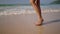 Black woman feet walking on sandy ocean beach at exotic island along sea water waves. Dark skin female legs go by surf