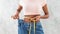 Black woman in old big jeans measuring her waist, showing results of slimming diet or liposuction, grey background