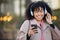 Black woman, texting and phone in city with headphones, smile and social media chat. Gen z businesswoman, smartphone and