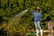 Black woman wearing a hat and rain boots tending to a garden while watering the plants