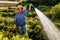 Black woman wearing a straw hat tending to her garden, watering the plants with a hose