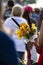 Black womans arm and hand as she holds a boquet of flowers with stems wrapped in plastic as a blurred unrecognizable crowd of peop