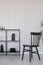 Black wooden chairs next to metal shelf with vases, plate and accessories on empty wall wall with unique wallpaper, real photo