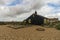 Black Wooden Cottage on Pebble Beach with Bright Blue Sky and Clouds