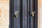 Black wooden door with brass vintage knockers as dolphin with a trident-shaped tails and Maltese cross