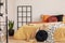 Black wooden grille next to the bed with orange bedding in the bedroom with white walls