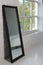 Black wooden rectangular vertical framed mirror beside big window