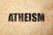 Black word Atheism on beige textured background. Philosophical or religious position