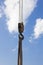 Black and yellow cargo crane hook with slings, against a blue sky with clouds