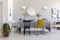 Black and yellow chair at table in white dining room interior with plants, lamps and mirror