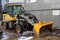 A black and yellow wheeled tractor stands against a wall of a house. Heavy construction machinery concept