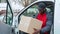 Black young adult delivery guy in work uniform sitting in door of white van looking at cardboard box parcel.