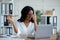 Black young businesswoman having tired irritated eyes, sitting at desk with laptop, exhausted from online work in office