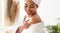 Black Young Woman Applying Moisturizer Cream On Shoulders In Bathroom