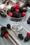 Blackberries and raspberries in a glass container on a wooden background. Textile. Wild flowers, daisies. Vertical position of the