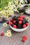 Blackberries and raspberries in a white container on a wooden background. Textile. Wild flowers, daisies. Vertical position of the