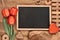 Blackboard framed with red tulips onl wooden background, space for your text