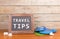 blackboard with text & x22;Travel tips& x22;, flops, seashells on brown wooden background