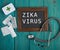 Blackboard with text & x22;Zika virus& x22;, pills and stethoscope on blue wooden background