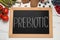 Blackboard with word Prebiotic and different products on white marble table, flat lay