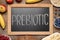 Blackboard with word Prebiotic and different products on wooden table, flat lay