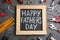 Blackboard with words HAPPY FATHER`S DAY and tools on stone background, flat lay