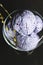 Blackcurrant and lavender ice cream with a lavender flower decoration in a ceramic glass on black background.