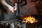 blacksmith holds red-hot metal by tongs in the forge furnace