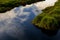 Blackwater marsh and river with grassy hillocks and reflections of white clouds