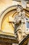 Blade nosed Roman statue in toga standing in front of ancient buildings with a pigeon roosting on his head -