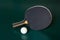 Blak ping-pong racket and a ball on a green table