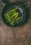Blanched broccoli in black cooking pan on wooden background, top view with copy space. Vertical.