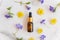 Blank amber glass essential oil bottle with pipette on marble background decorated blooming wild flowers. Skin care concept with