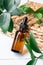 Blank amber glass essential oil bottle with pipette on wooden background decorated green leaves. Skin care concept with natural