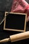 Blank, empty, black chalkboard with wooden rolling pin, wire whisk and red checkered dish towel flat lay from above on black