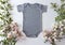 Blank Gray Baby Grow On An Off White Background With Green Leaves and Pink Roses