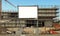 Blank information board near the construction site with a new concrete building among scaffolding