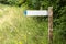 A blank metal arrow pointing left, bolted to a wooden pole in the woods.