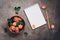 Blank notepad, ceramic bowl with flowers of coral roses and pencil on a dark rustic background.. Top view, flat lay feminine