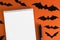 Blank notepad on orange background with paper bats silhouettes, traditional Halloween decor. The concept of planning and