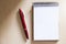 Blank notepad on the wooden table, with a red pen at the side, with sunlight hitting the side.