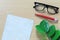 Blank paper note and eyeglasses placed on a brown wooden floor.