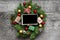 Blank photo frame in christmas wreath with decorations and gift boxes on rustic wooden table