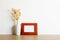 A blank photo frame with natural brown flowers over the wooden table.