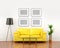Blank pictures on the white wall weigh over the yellow sofa.