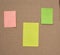 Blank pink, yellow and green papers glued on a brown cardboard surface