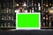 Blank screen of laptop on blur alcohol drink bottle on bar counter in the dark night background.