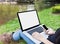Blank screen laptop with girl sitting on grass field at riverside, girl or women with smartphone in hand surfing internet in