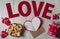 A blank sheet of paper, an envelope, a gift box, homemade cookies, wooden letters and red hearts on a light wooden background.