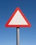 Blank triangle warning road sign on post with blue sky background. UK